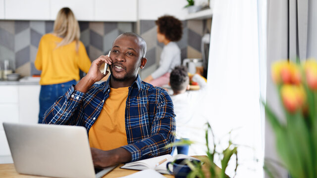 Man with wife and children using laptop and smartphone, working in home office.