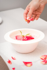 Beautician's female hands preparing manicure bath with red and pink roses petals on the table in spa