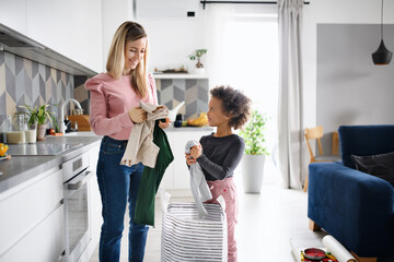 Mother with small daughter doing the laundry in kitchen at home.