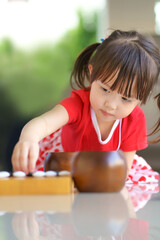 little cute asian girl playing black stone to the  wooden baduk (GO) board game