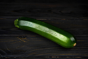 One fresh green zucchini on a dark wooden background