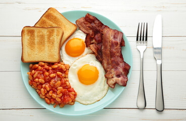 Traditional full English breakfast - fried eggs, beans, bacon and toast on white table.