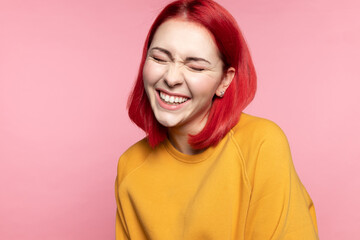 Fototapeta premium Headshot of cheerful modern young girl with dyed pink hairs, laughing closed eyes at funny joke feels overjoyed having wide snow-white smile straight teeth posing on rose studio background.