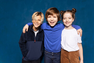 Diverse smiling classmates best friends look at camera together on blue background. Schoolchildren...