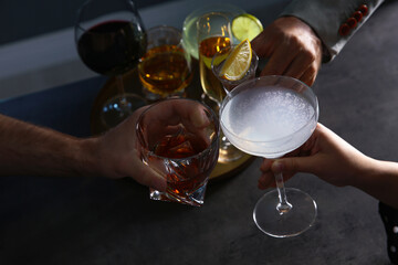 People with different alcohol drinks clinking glasses indoors, closeup