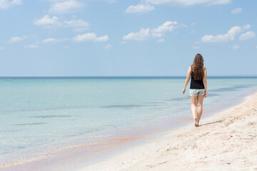 Fototapeta na wymiar Young woman walking along the sea beach