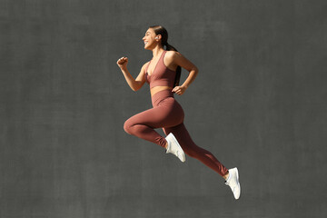 Fototapeta na wymiar Young woman in stylish sports wear jumping on grey background