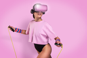 Beautiful young caucasian sportswoman in pink colored sport t-shirt with black body - Studio shooting during gymnastics workout doing exercise wearing hi tech futuristic vr glasses and jumping rope