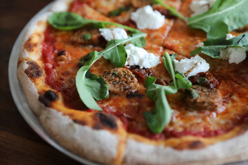 Italian Sausage and rocket salad pizza on wood background