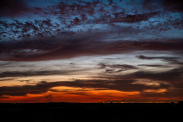 Obraz premium Nubes en el atardecer con ciudad y montañas en el horizonte