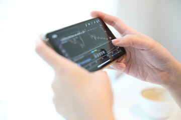Female hand with smartphone trading stock online in coffee shop , Business concept