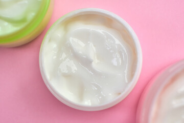 face cream in open multi-colored jars on pink background