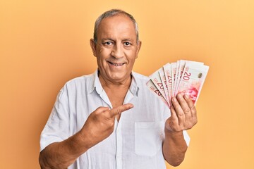 Handsome mature man holding 20 israel shekels banknotes smiling happy pointing with hand and finger