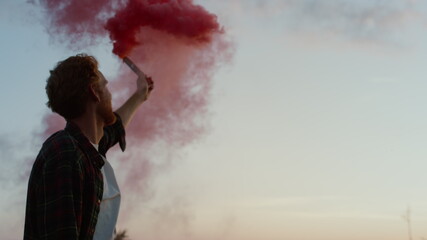 Man holding smoke grenade. Happy guy celebrating victory on top of mountain