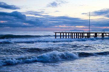 Obraz premium View from beach to water of sea, waves with white foam, pierce and sky with clouds in a nice evening.