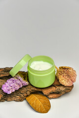 Face cream in green jar on tree bark, white background.
