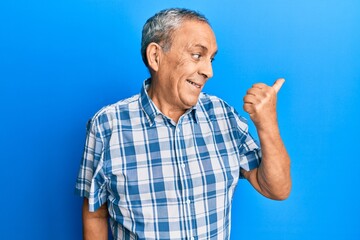 Senior hispanic man wearing casual clothes pointing thumb up to the side smiling happy with open mouth