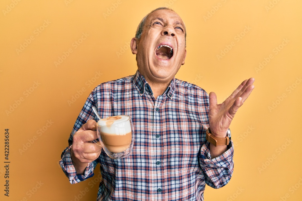 Sticker handsome senior man with grey hair drinking a cup coffee crazy and mad shouting and yelling with agg