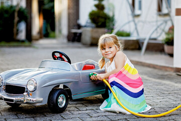 Little toddler girl playing with big vintage toy car and having fun outdoors in summer. Cute child...