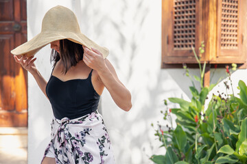 Young woman hides her face from the rays of the sun under a large straw hat.