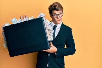 Handsome caucasian business man holding briefcase full of dollars skeptic and nervous, frowning...