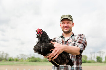 a young male farmer with a chicken in his hands stands in his garden in the village. © Kolomiiets Viktoriia