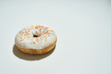Freshly baked delicious donut with colorful sprinkles and white sugar glaze isolated on light background, copy space for text