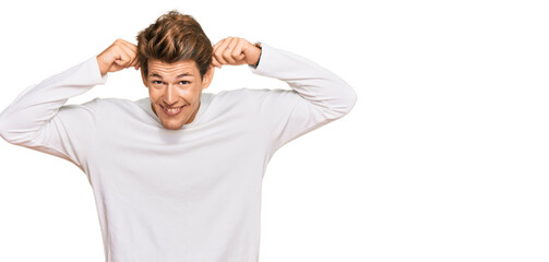 Handsome caucasian man wearing casual white sweater smiling pulling ears with fingers, funny...
