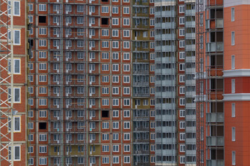 Fototapeta premium Construction of a residential multi-storey building. Windows, balconies. Concrete, brick walls. Blue, white, brown colors.