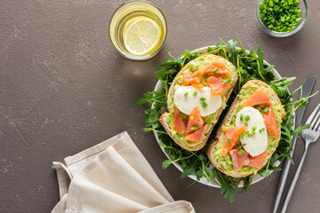 Delicious hearty breakfast, sandwiches with avocado paste, salmon and mozzarella on a plate with arugula and pea sprouts