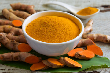 Turmeric powder in a white bowl and fresh turmeric (curcumin) on wooden background,Used for cooking.