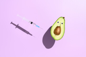 Concept of vaccination against coronavirus. Funny half an avocado and a syringe with vaccine against COVID-19, levitating over purple background. Minimalistic creative image with copy space