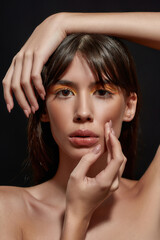 Naklejka premium Beauty portrait of fashionable young brunette female model with colorful orange makeup looking at camera, posing with hands near her face isolated over black background