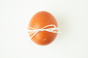 Brown egg wrapped with thread on white background with copy space