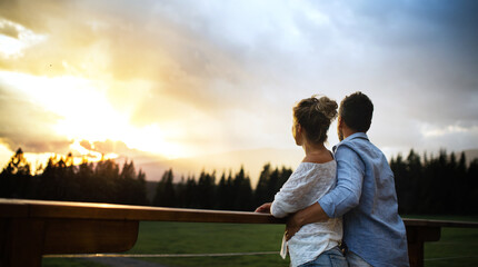 Rear view of couple standing on patio of wooden cabin at sunset, holiday in nature concept.