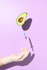 Coronavirus Vaccine and vaccination concept. Half an avocado and a syringe with vaccine against COVID-19, balancing on a hand in a medical glove. Minimalistic creative visual on a purple background