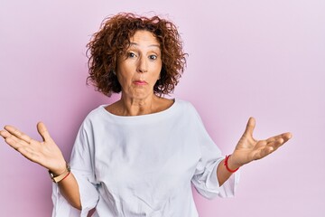 Beautiful middle age mature woman wearing elegant clothes over pink background clueless and...