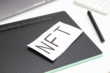Graphic tablet, stylus, computer and paper with the inscription on it: NFT. Workspace