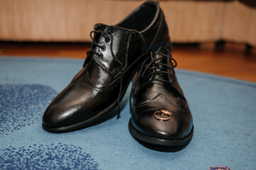Gold wedding rings on black shoes on the floor. Accessories for the groom on the wedding day