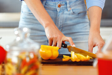 Woman cuts yellow bell pepper for salad on wooden table