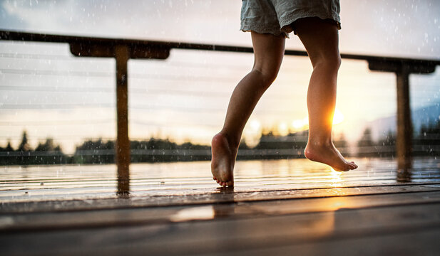 Unrecognizable small daughter playing in rain on patio of wooden cabin, holiday in nature concept.