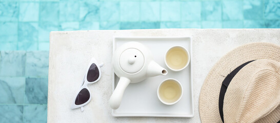 white sunglasses, hot tea pot and hat near swimming pool in luxury hotel. Summer travel, vacation, holiday and weekend concept