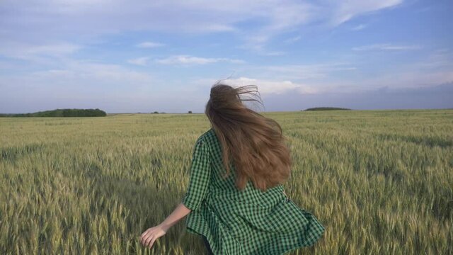 Beautiful teenage girl with long hair in the park. A young girl runs through a wheat field. Happy, free young girl in green wheat. Hair develops in the wind.