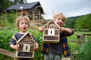 Small boy and girl holding bug and insect hotel in garden, sustainable lifestyle.