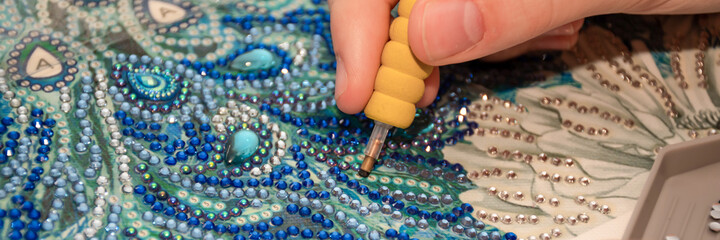 Diamond painting embroidery craft. Acrylic rhinestones and a pen. Closeup, selective focus
