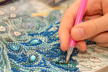 Diamond painting embroidery craft. Acrylic rhinestones and a pen. Closeup, selective focus