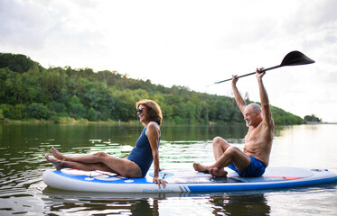 Senior couple paddleboarding on lake in summer.