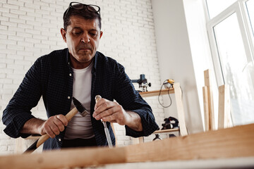 Middle-aged man carpenter working in a workshop with chisel and hammer