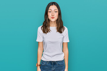 Young beautiful woman wearing casual white t shirt puffing cheeks with funny face. mouth inflated...