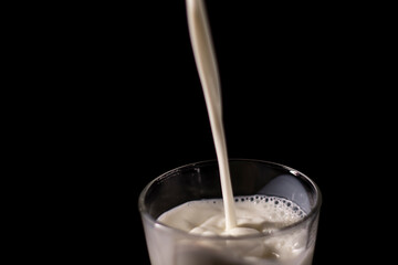 pouring milk in a glass. splash of white liquid isolated on dark background